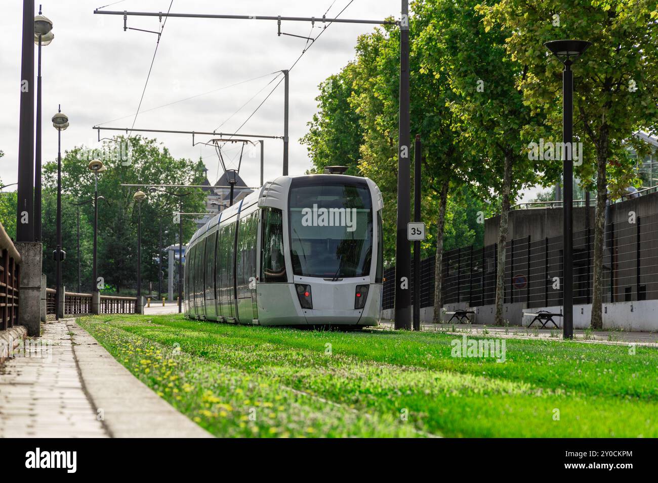 Tram su una pista del tram. Percorso del tram attraverso l'erba a parigi. Trasporto ferroviario in tram a parigi, binari del tram disposti in un'erba verde accanto a una strada trafficata. Foto Stock