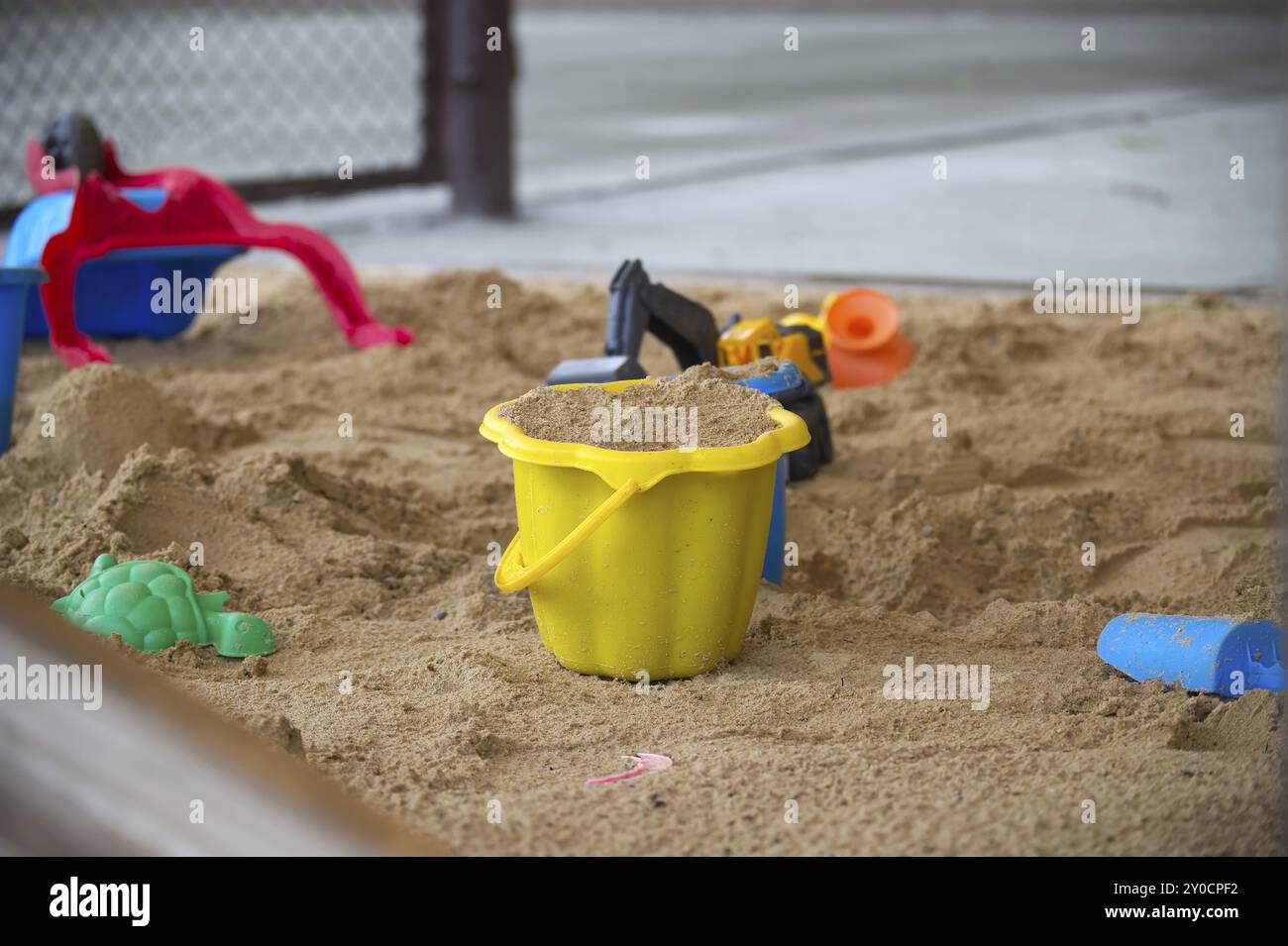 Giocosa scena all'aperto in spiaggia o parco giochi, concentrandosi su un secchio marrone pieno di sabbia e circondato da giocattoli Foto Stock