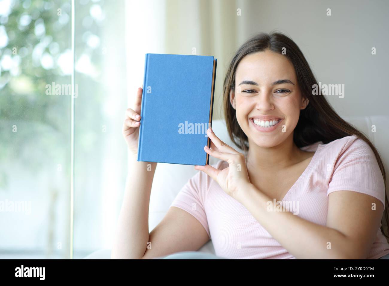 Donna felice che mostra alla fotocamera la copertina del libro di carta bianca a casa Foto Stock