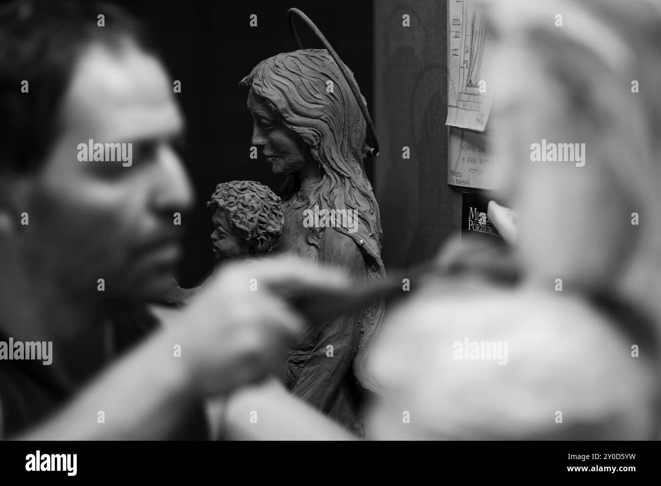 Primo piano delle mani di un artista mentre lavora su una statua di legno, utilizzando uno scalpello per modellare il legno con precisione. L'immagine in bianco e nero acquisisce Foto Stock