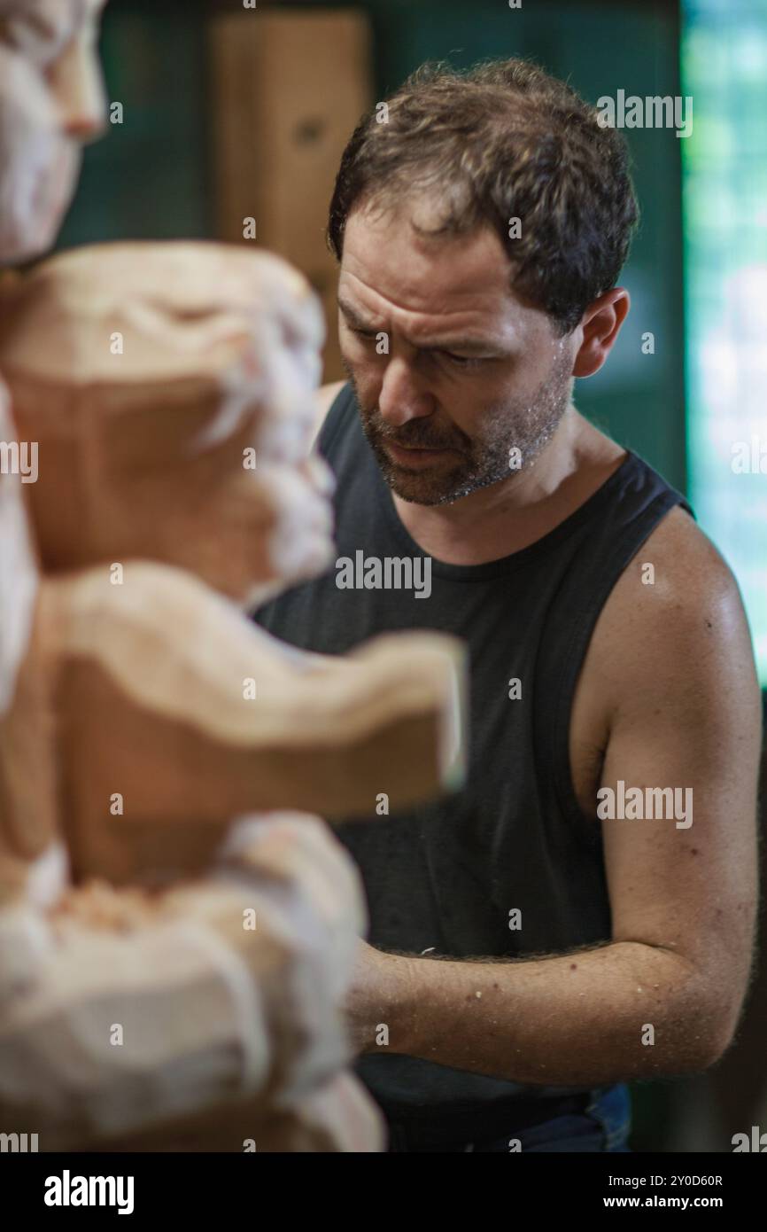 Un falegname incentrato sta lavorando su una scultura religiosa in legno nella sua bottega, utilizzando uno scalpello per intagliare i dettagli del legno Foto Stock