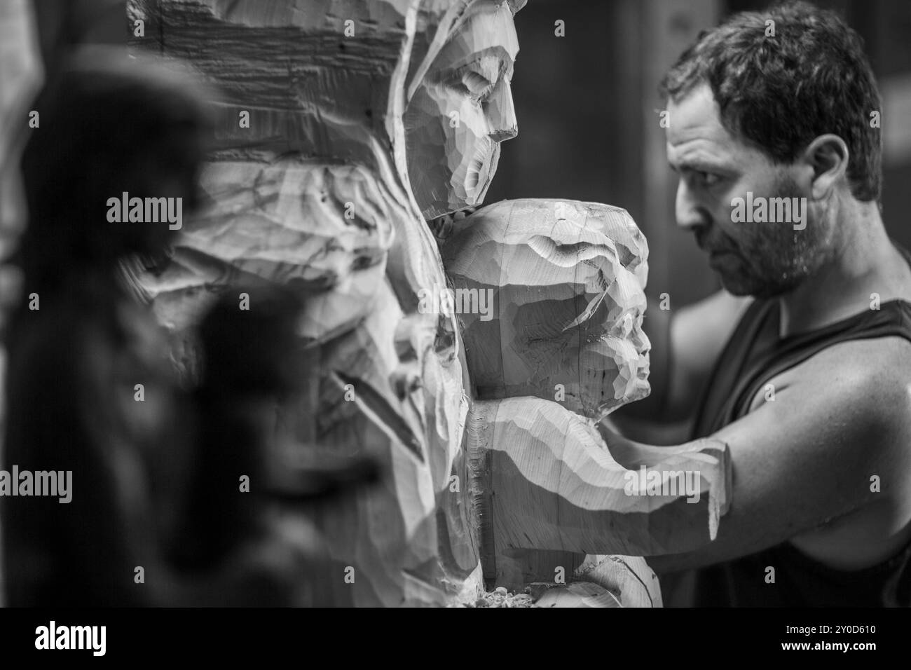 Primo piano delle mani di un artista mentre lavora su una statua di legno, utilizzando uno scalpello per modellare il legno con precisione. L'immagine in bianco e nero acquisisce Foto Stock