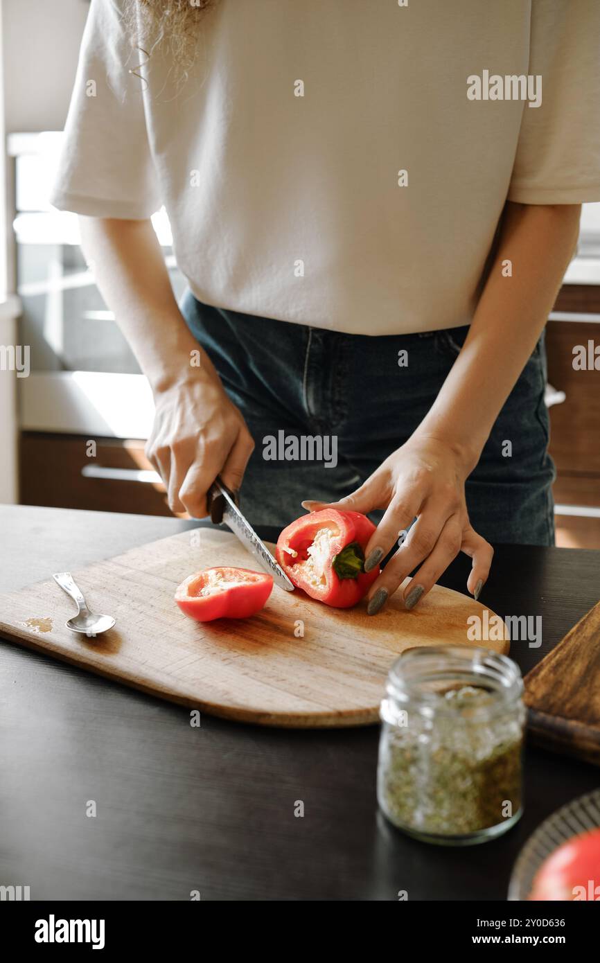 Donna irriconoscibile che taglia succoso peperone su un tagliere in cucina Foto Stock