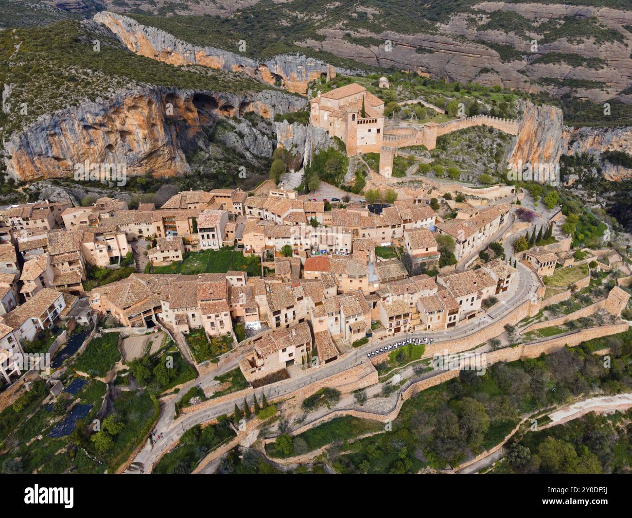 Un pittoresco villaggio medievale con un'imponente fortezza e mura fortificate, annidato tra le montagne, vista aerea, chiesa collegiata sulla collina, Foto Stock