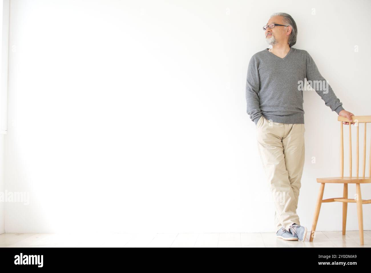 Un uomo anziano in piedi con la mano su una sedia Foto Stock