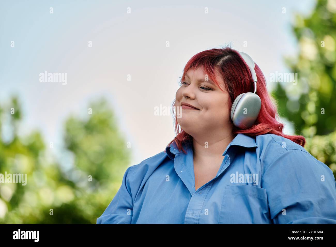 Una donna di grandi dimensioni con i capelli rosa sorride mentre ascolta musica all'aperto. Foto Stock