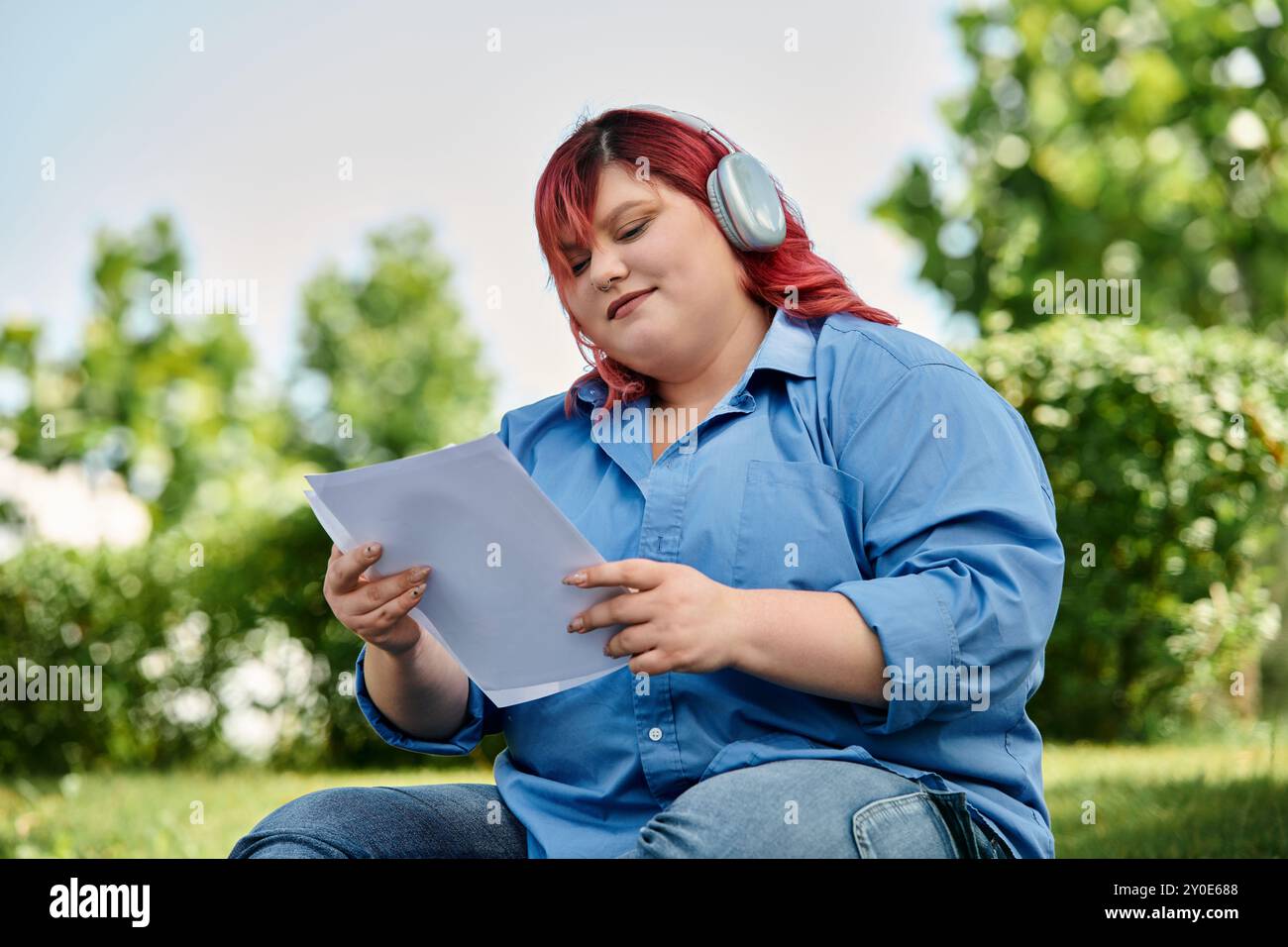 Una donna di grandi dimensioni con capelli rossi e cuffie legge una carta all'aperto. Foto Stock