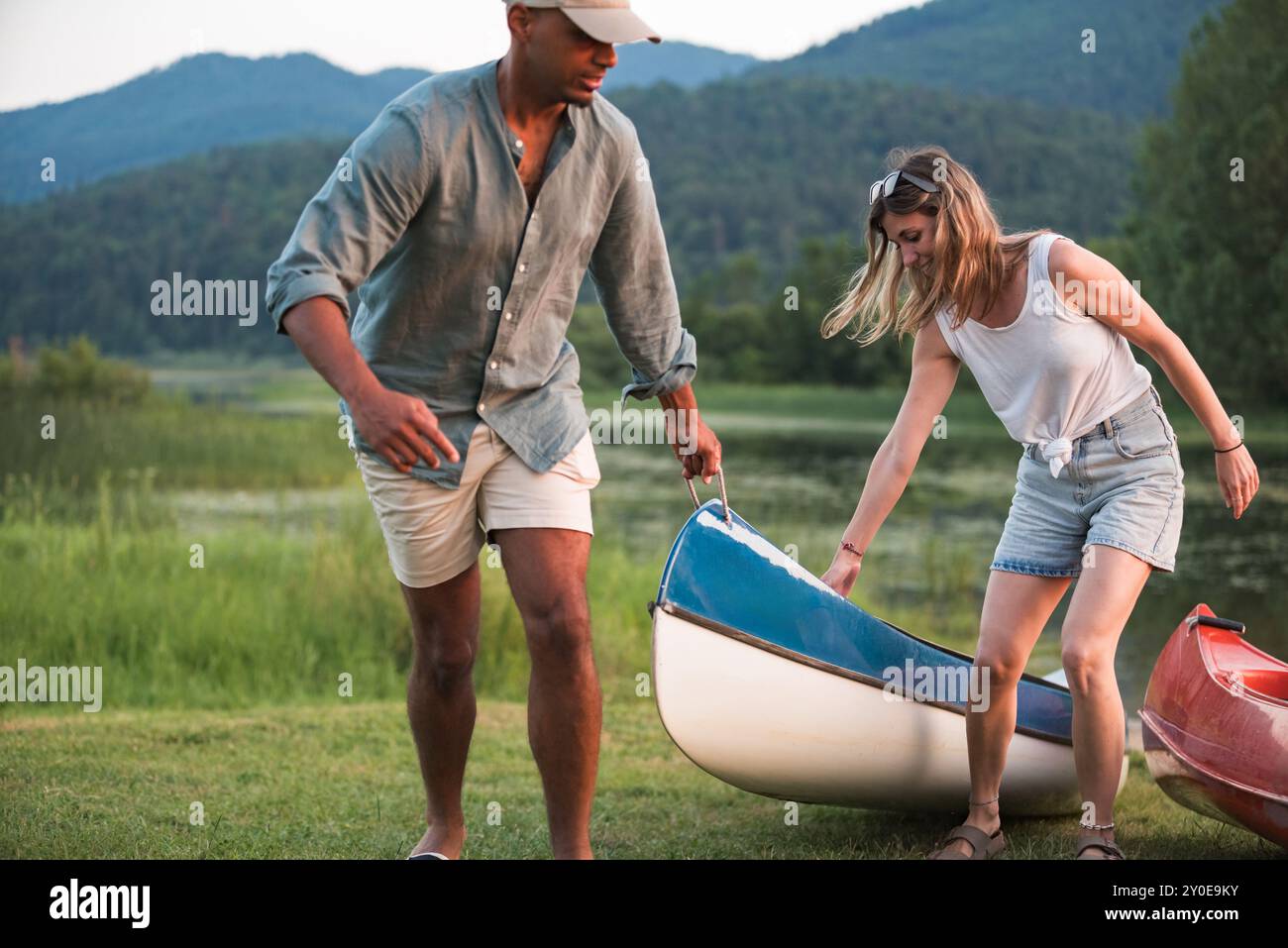 Coppia felice che si gode l'estate sul lago mentre tira la canoa fuori dall'acqua Foto Stock