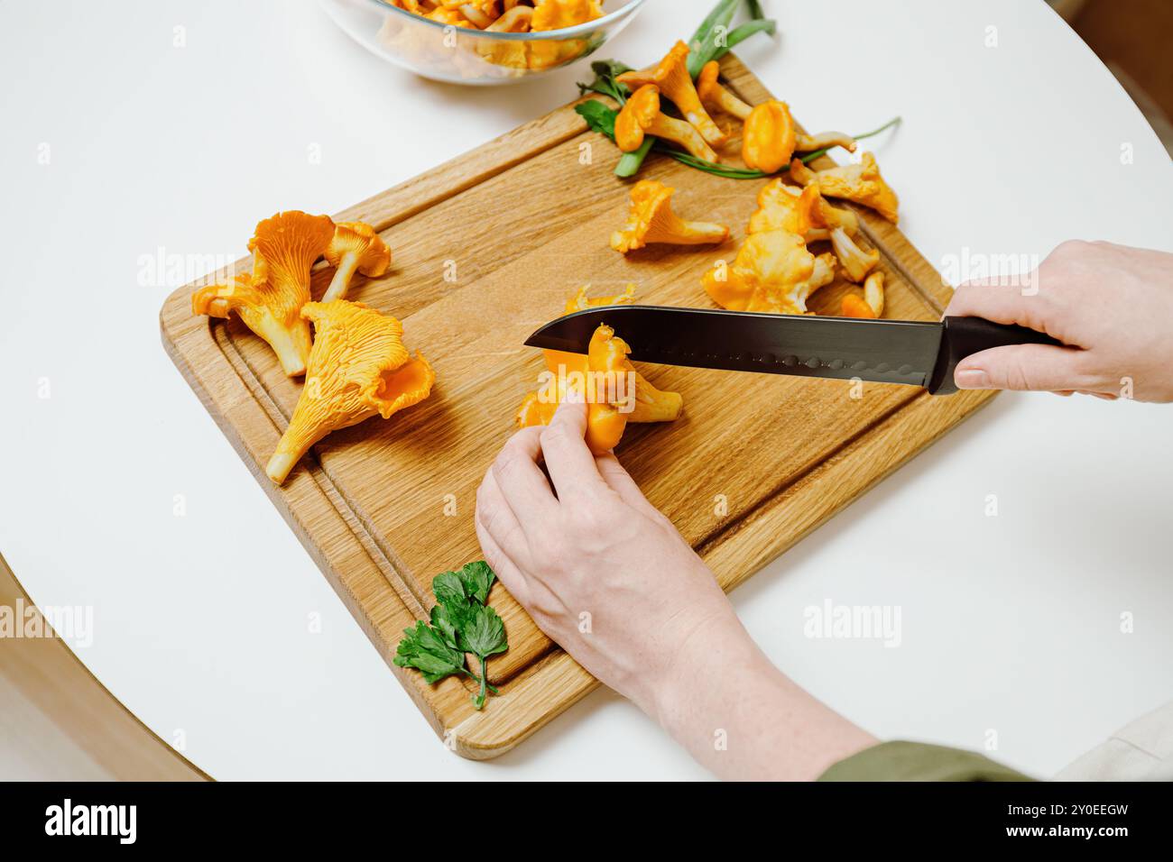 Lo chef trita freschi funghi chanterelle su un tagliere di legno, preparando salutari ingredienti di stagione Foto Stock