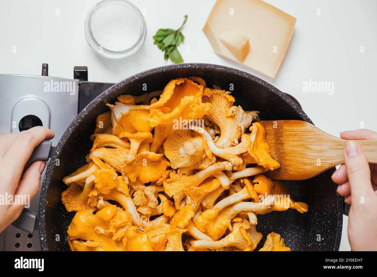 Vista dall'alto dei funghi canterelle dorati che mescolano in padella con spatola di legno, avvicinano molti funghi con consistenza visibile Foto Stock