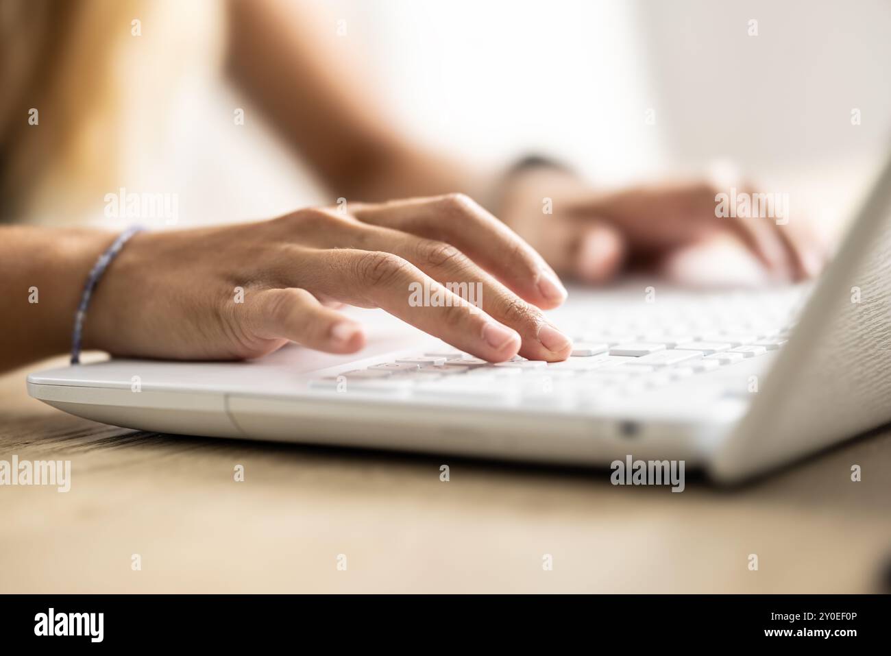 Le mani femminili scrivono sulla tastiera del laptop navigando su Internet e facendo tex-ting agli amici tramite social network, seduti a un tavolo di legno all'interno. Tecnologia e c Foto Stock