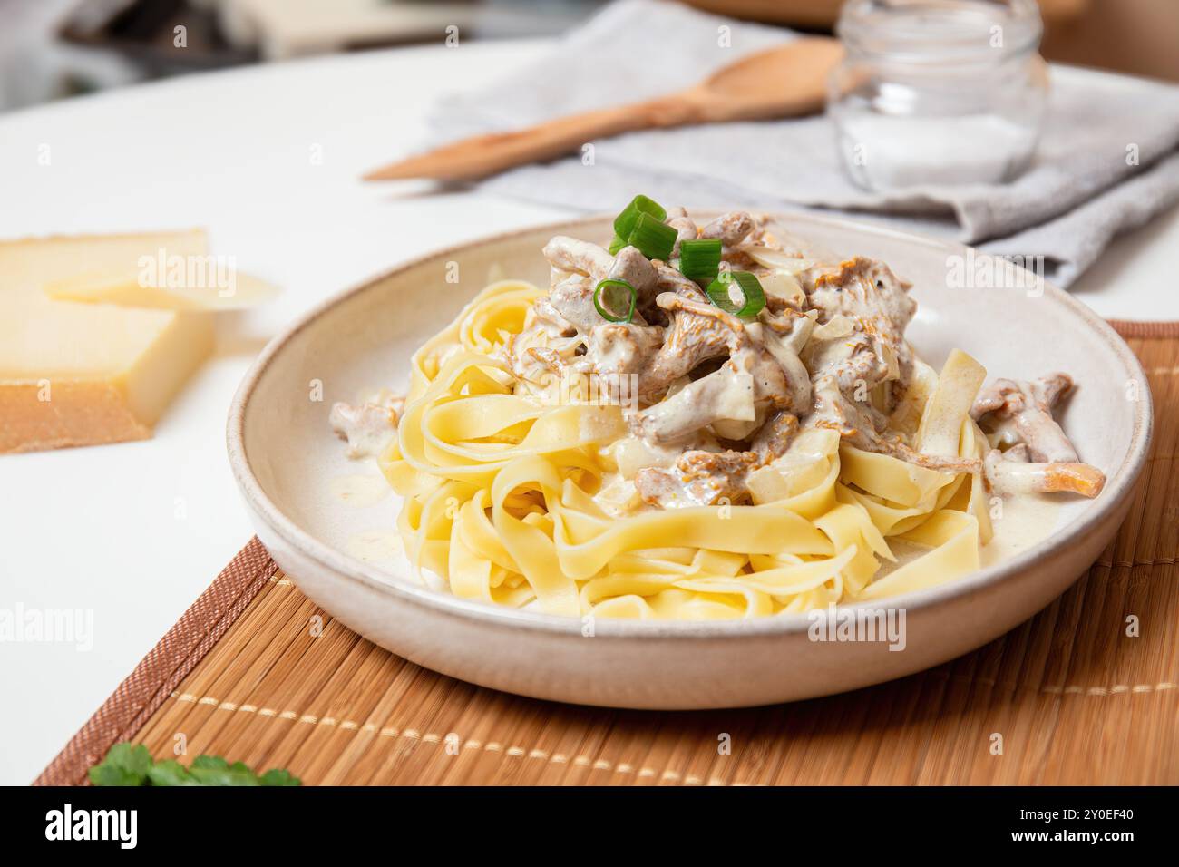 Un delizioso piatto di tagliatelle cremose condite con funghi chanterelle e cipolle verdi, servite con formaggio sul tavolo Foto Stock