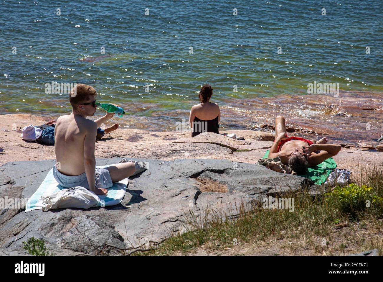 Vigilia di mezza estate in città. Persone che prendono il sole su una roccia vicino al mare nel quartiere Eira di Helsinki, Finlandia. Foto Stock