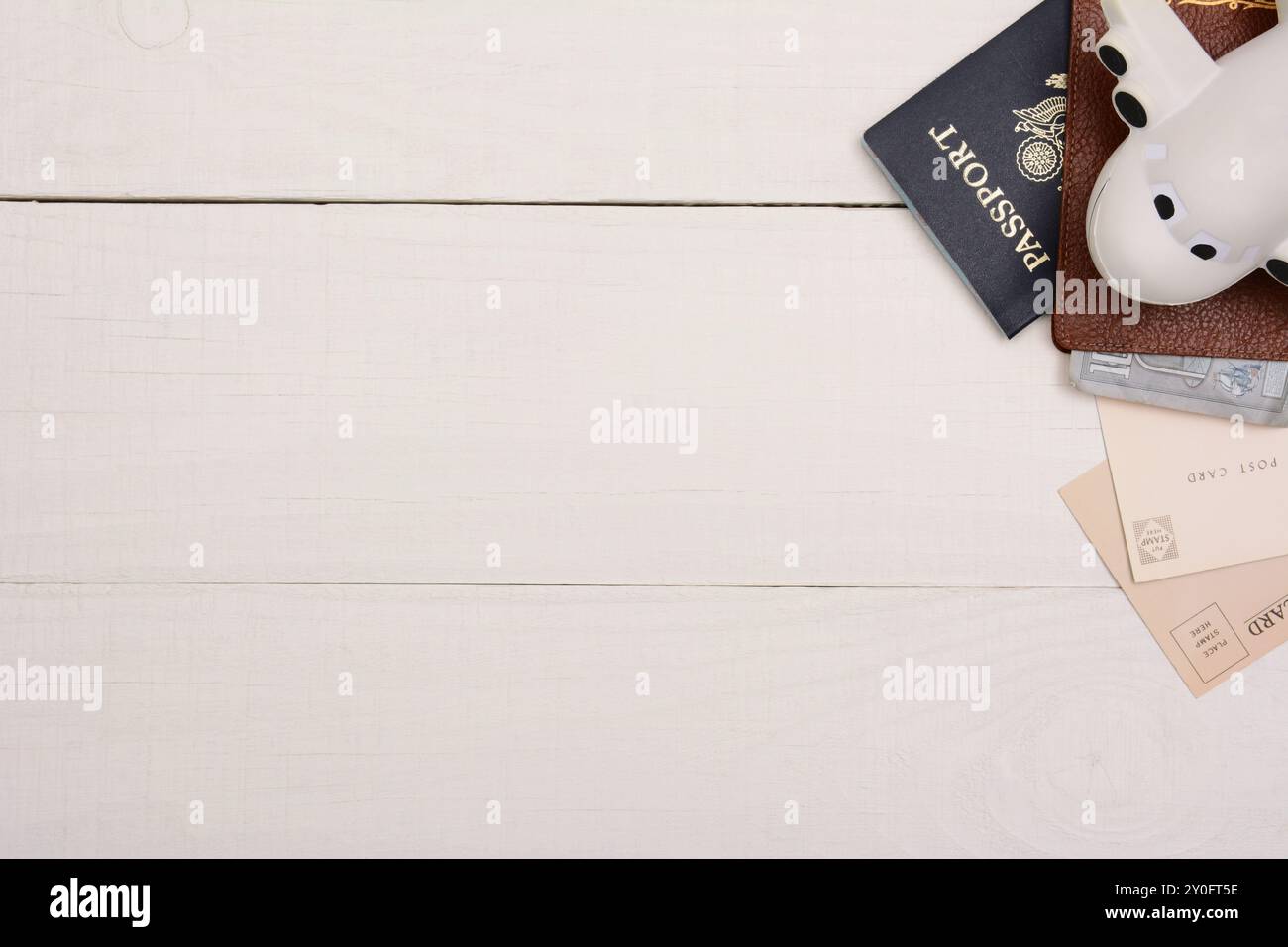 Viaggia la natura morta su un tavolo di legno bianco. Passaporto, aereo giocattolo, portafoglio con denaro e cartoline nell'angolo superiore destro su un tavolo di legno bianco con c Foto Stock