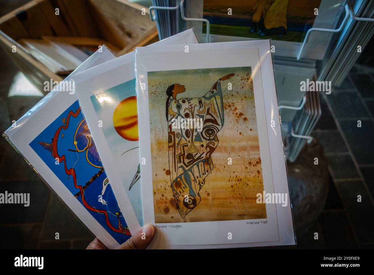 Una mano che tiene stampe d'arte indigene all'interno di un negozio di articoli da regalo, che mostra opere d'arte culturali disponibili per l'acquisto, riflettendo il ricco patrimonio di Indigenou Foto Stock
