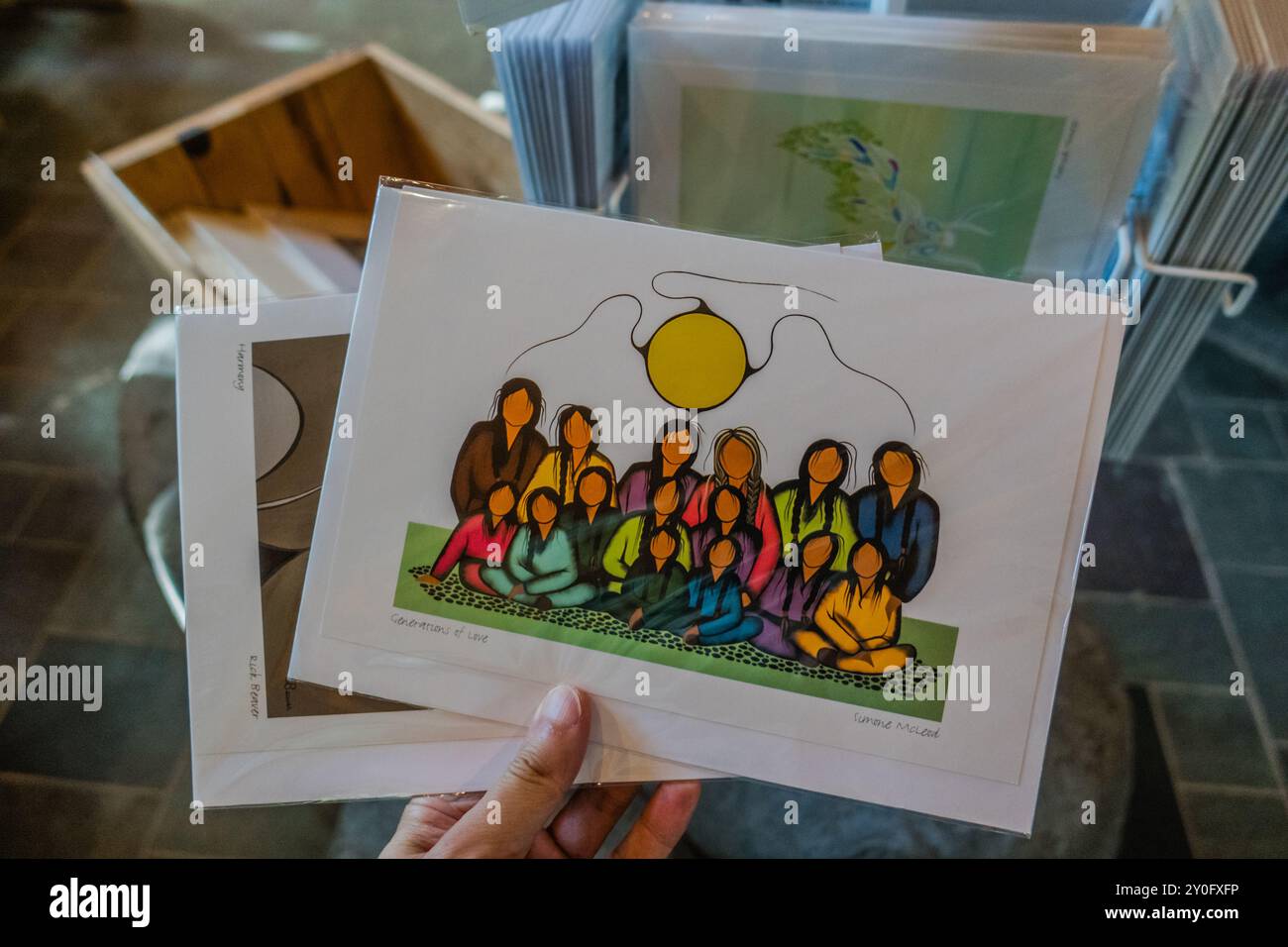 Una mano che tiene stampe d'arte indigene all'interno di un negozio di articoli da regalo, che mostra opere d'arte culturali disponibili per l'acquisto, riflettendo il ricco patrimonio di Indigenou Foto Stock