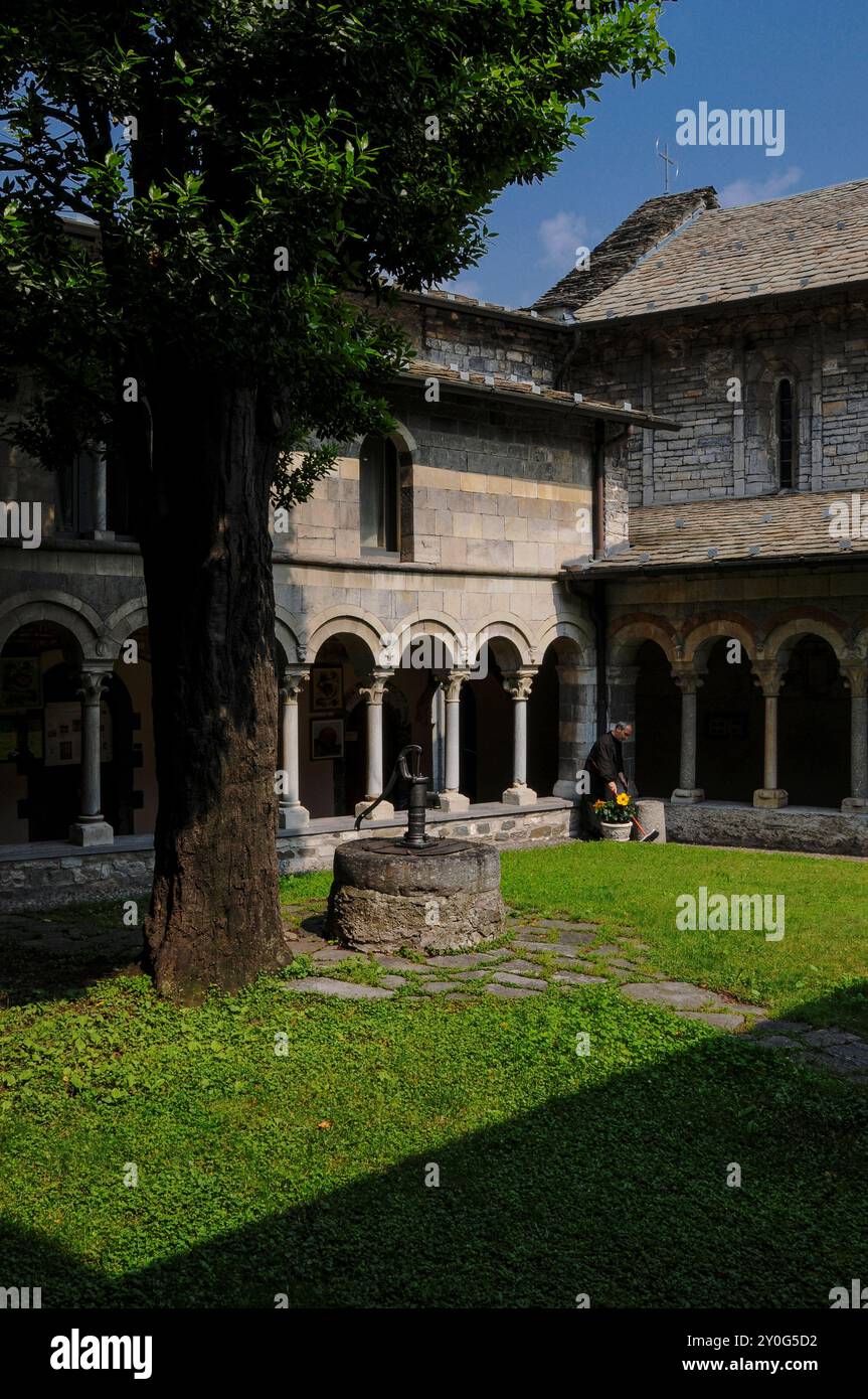 Angolo del chiostro, costruito intorno al 1242, presso l'Abbazia di Piona, Colico, Lombardia, Italia. Il chiostro è annesso alla chiesa abbaziale della Chiesa di San Nicola (a destra), che risale alla fine del 1000 o all'inizio del 1100 Davanti al chiostro si trova una testa di pozzo sormontata da una pompa manuale. Foto Stock