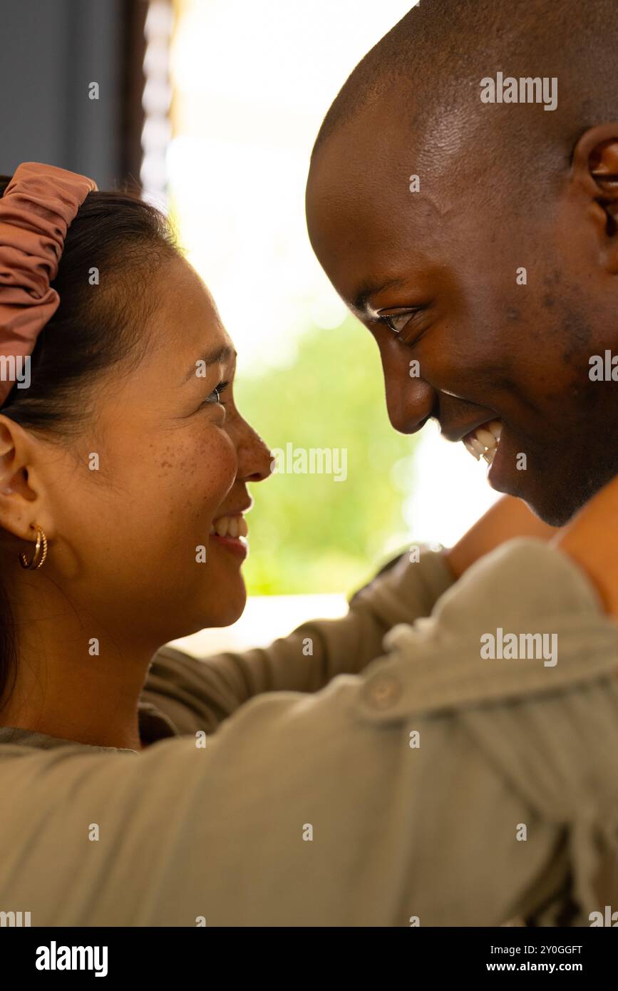 Coppia multirazziale sorridente che si abbraccia a vicenda, condividendo momenti teneri a casa Foto Stock