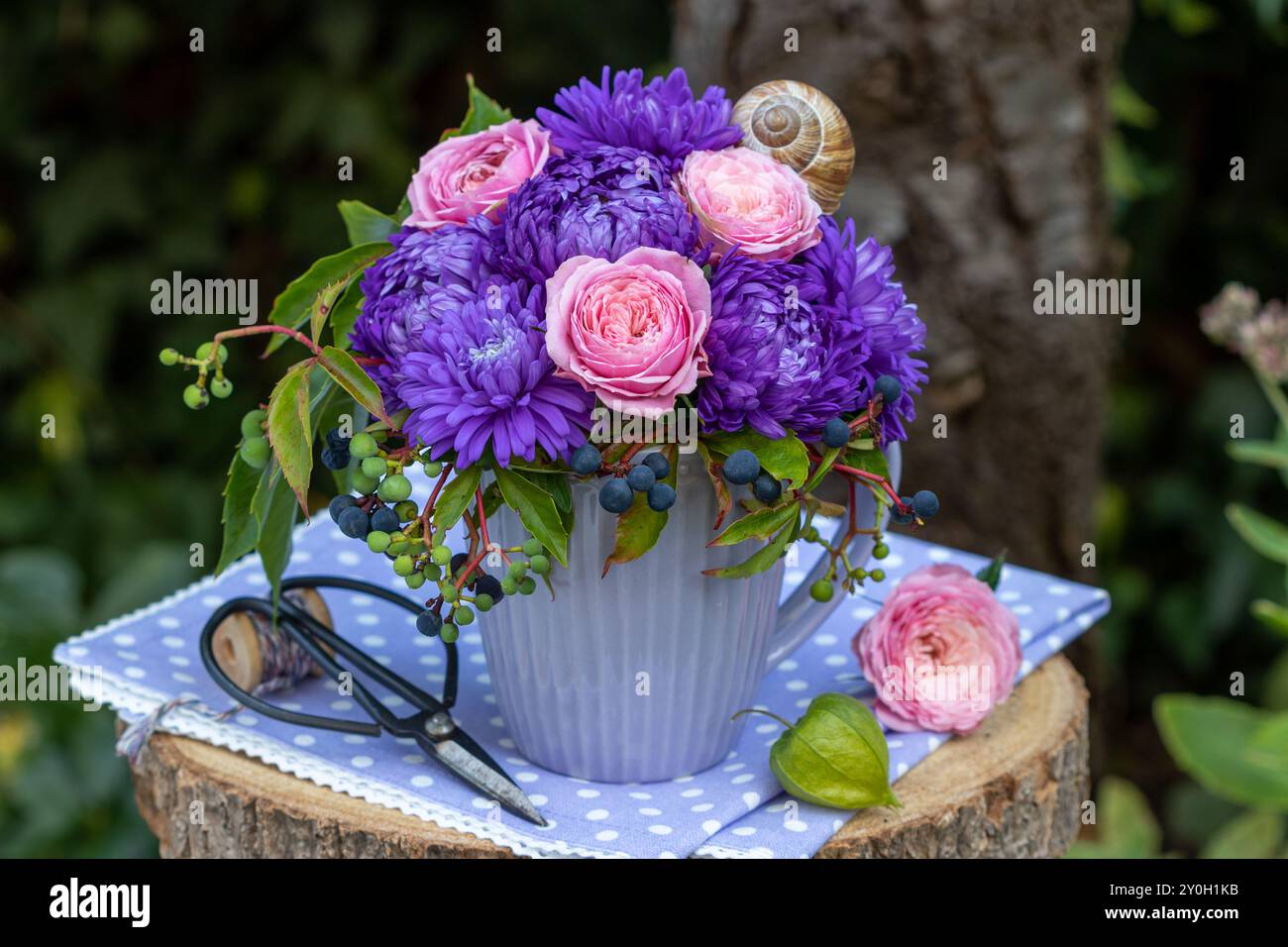 composizione floreale con rose rosa, ceramiche estive viola e crepuscolo della virginia in una tazza in giardino Foto Stock