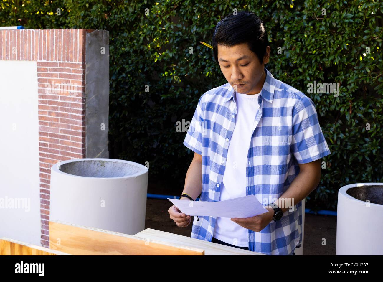 Revisione dei progetti, uomo asiatico in camicia a scacchi che lavora su progetti di costruzione all'aperto Foto Stock