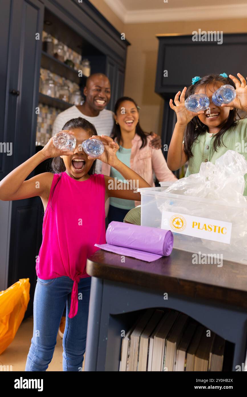 Riciclare bottiglie di plastica, bambini che giocano mentre i genitori sorridono in cucina Foto Stock