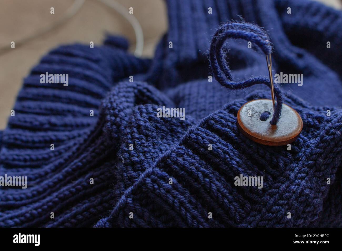 Cardigan in maglia di lana blu con bottone in legno e ago da cucire. Unione del modello di nervatura con i bottoni. Cardigan fatto a mano. Sfondo abiti caldi. Foto Stock