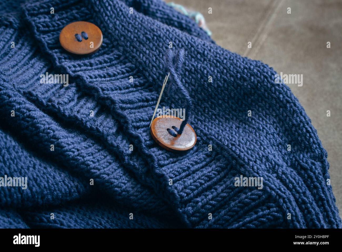 Cardigan in maglia di lana blu con bottone in legno e ago da cucire. Unione del modello di nervatura con i bottoni. Cardigan fatto a mano. Sfondo abiti caldi. Foto Stock
