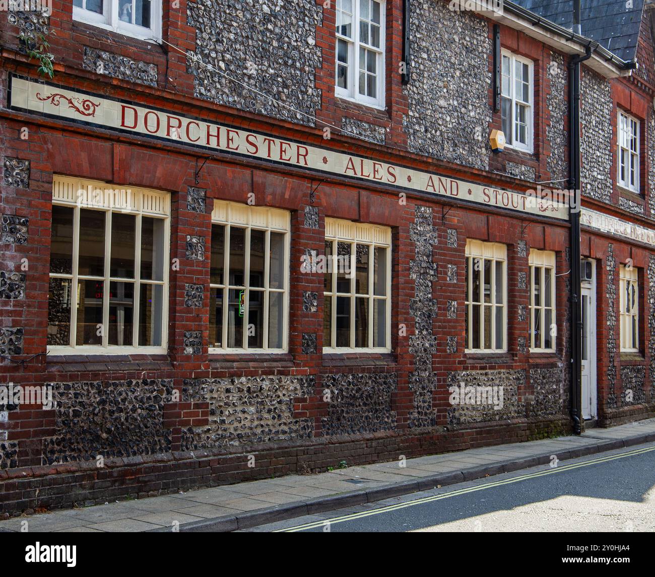 Edificio storico con facciata in pietra e mattoni che pubblicizza "Dorchester Ales and Stout" a Winchester, Regno Unito, in una giornata di sole Foto Stock