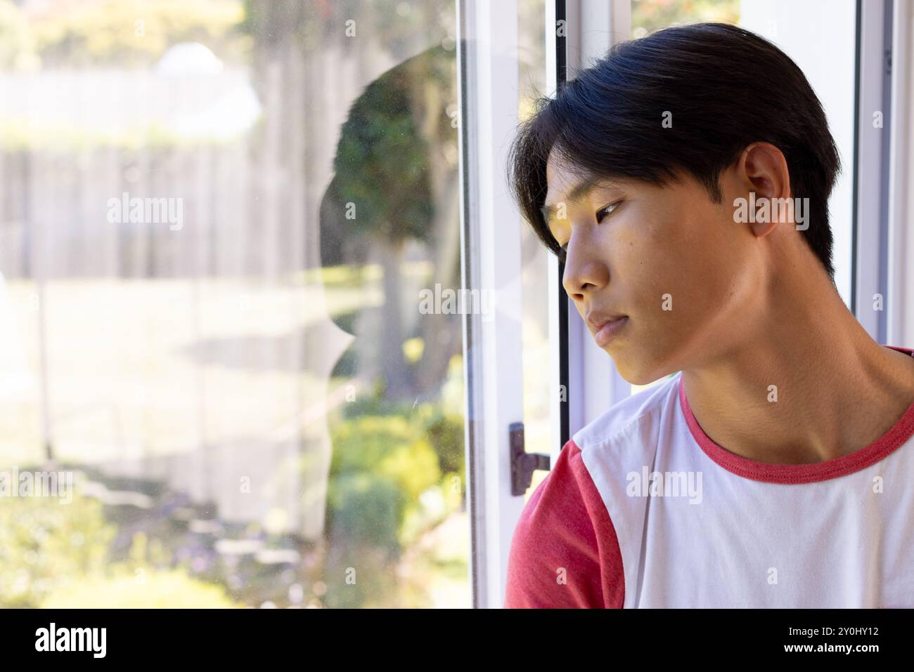 Guardando fuori dalla finestra, il giovane uomo asiatico che riflette, indossa camicia casual rossa e bianca, copia spazio Foto Stock