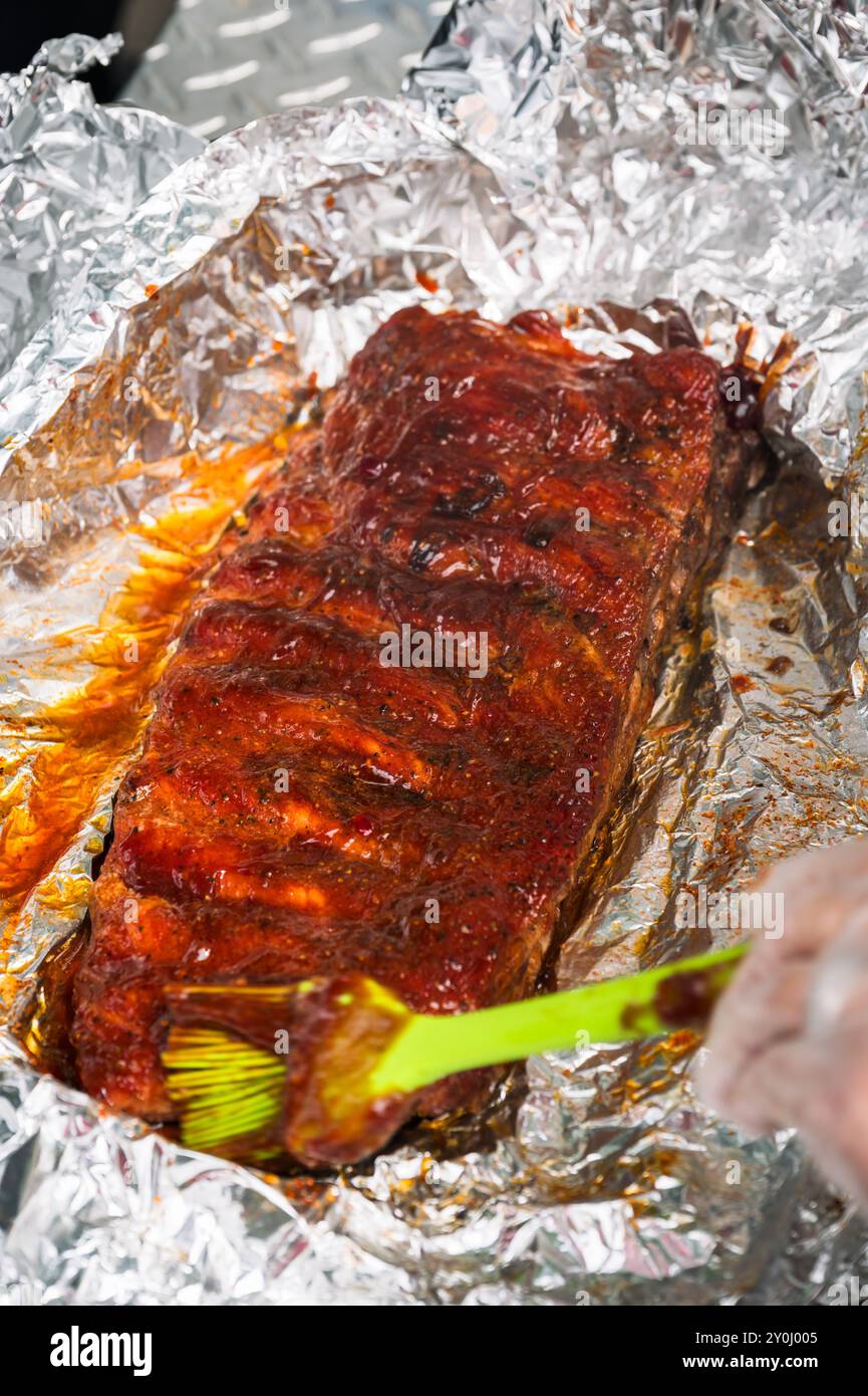 Un mercato agricolo del sabato mattina organizza una gara di barbecue sulla strada principale di Ellensburg, Washington, USA. Applicazione di salsa barbecue su una griglia di costolette. Foto Stock