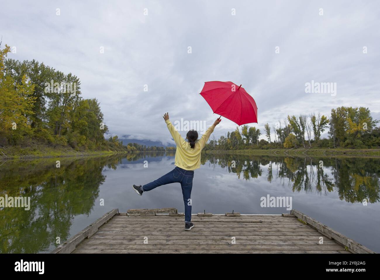 Una donna che tiene in mano un ombrello rosso si mette in posa mentre si trova su un molo vicino al fiume Kootenai nell'Idaho settentrionale Foto Stock