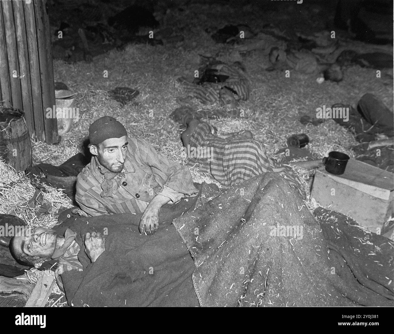 Due sopravvissuti si trovano tra i cadaveri sul pavimento coperto di paglia della caserma chiamata "Boelke Kaserne". A Nordhausen. Questo campo faceva parte del complesso di lavoro forzato Dora-Mittelbau. A Nordhausen i prigionieri furono lasciati a morire in squallore quando erano troppo deboli per lavorare. Nei suoi tre mesi di funzionamento, 3000 dei 6000 che erano lì morirono. Foto Stock