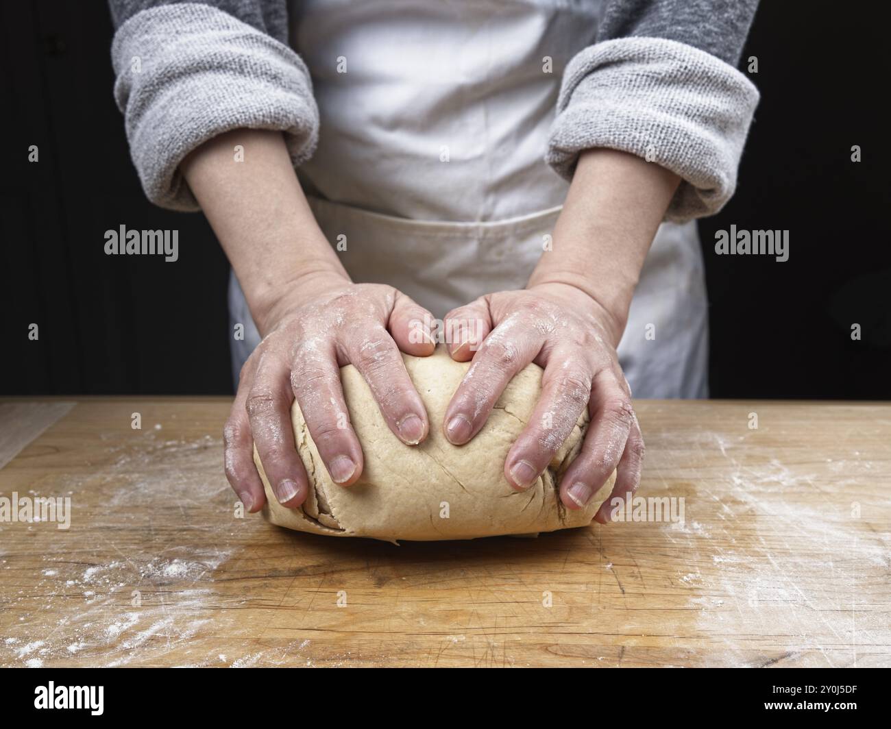 Una foto ravvicinata delle mani di una donna che impastano una grande palla di impasto su un tagliere di legno Foto Stock