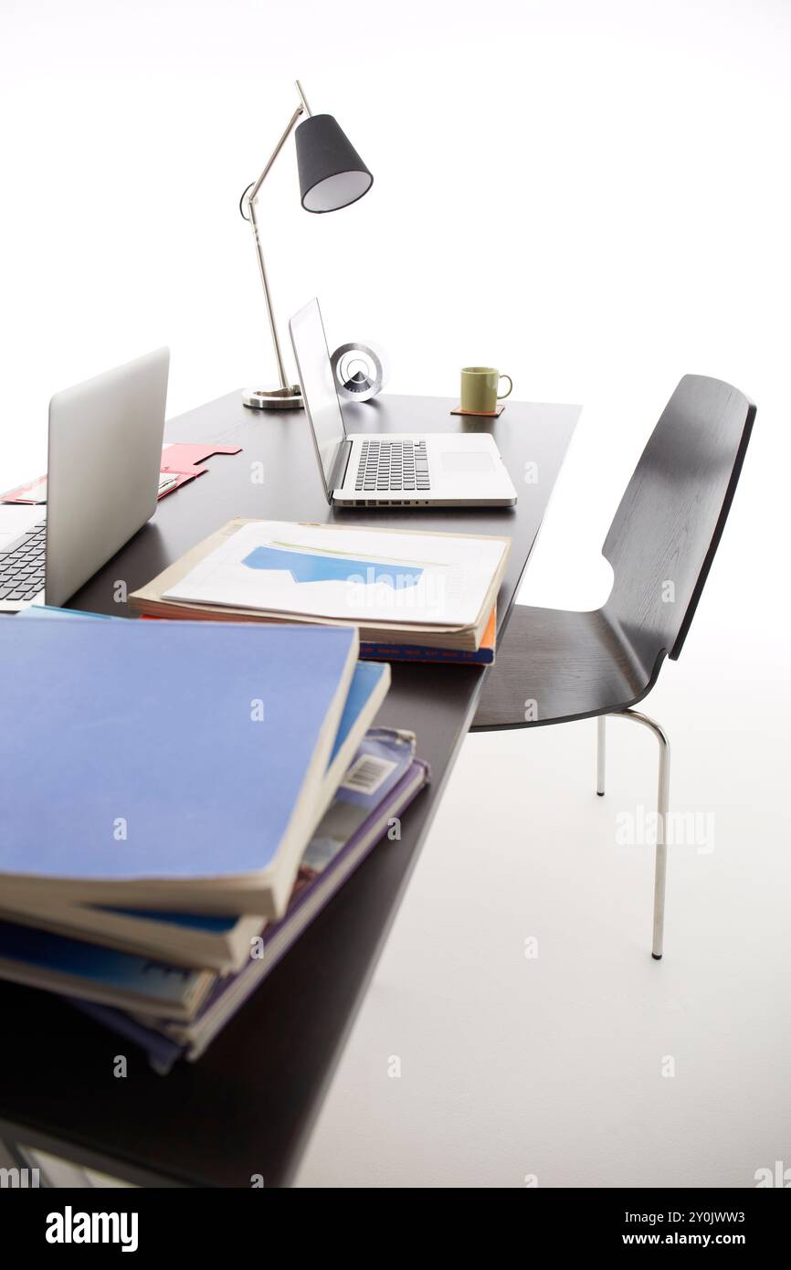 Due PC, libri, tazze da caffè e simili su una scrivania nera Foto Stock