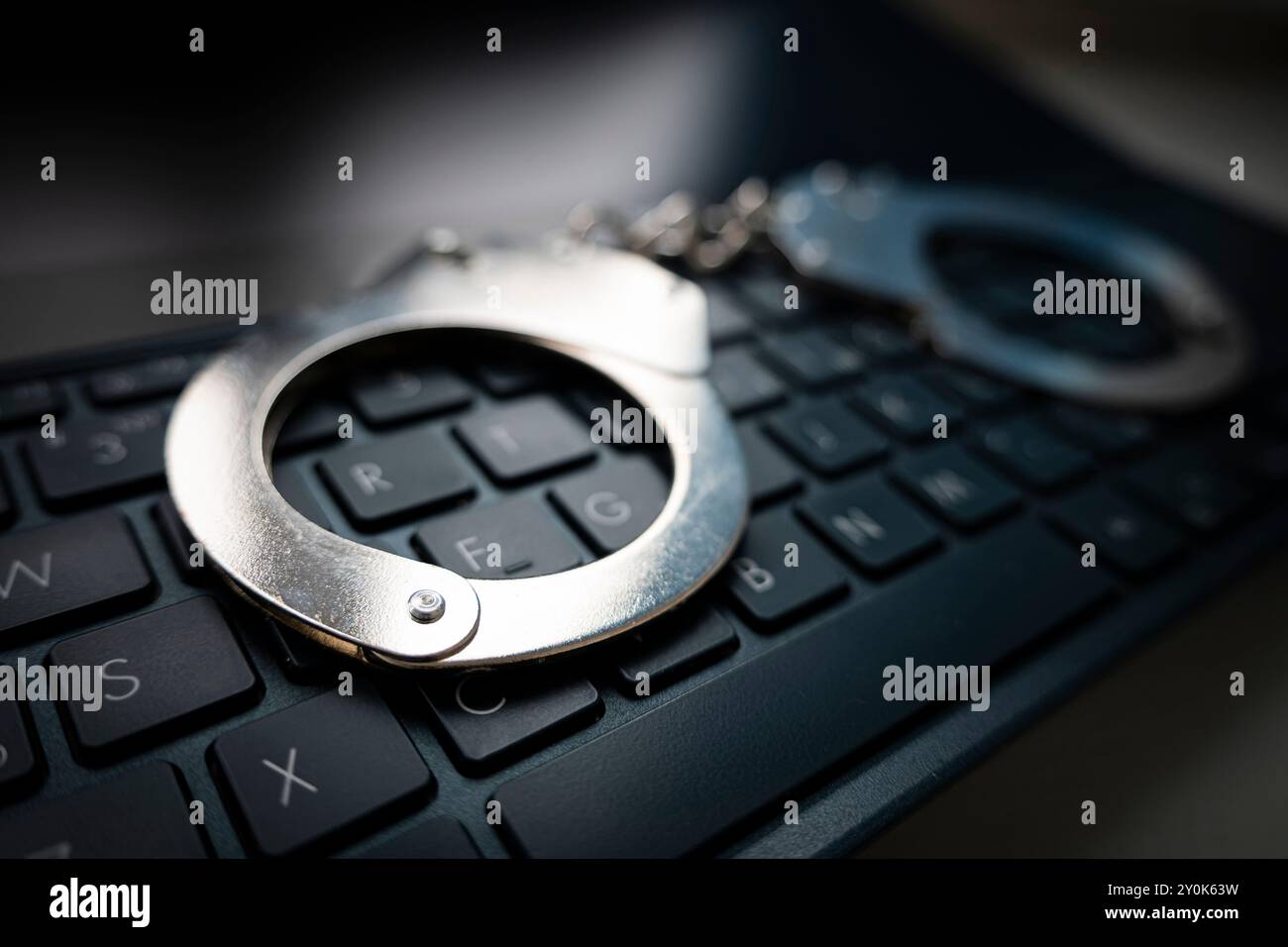 Attenzione selettiva alle manette su un concetto di cyber crimine, hacking, bullismo contro la legge con tono basso e scuro. polsini in metallo su un cinghiale nero Foto Stock