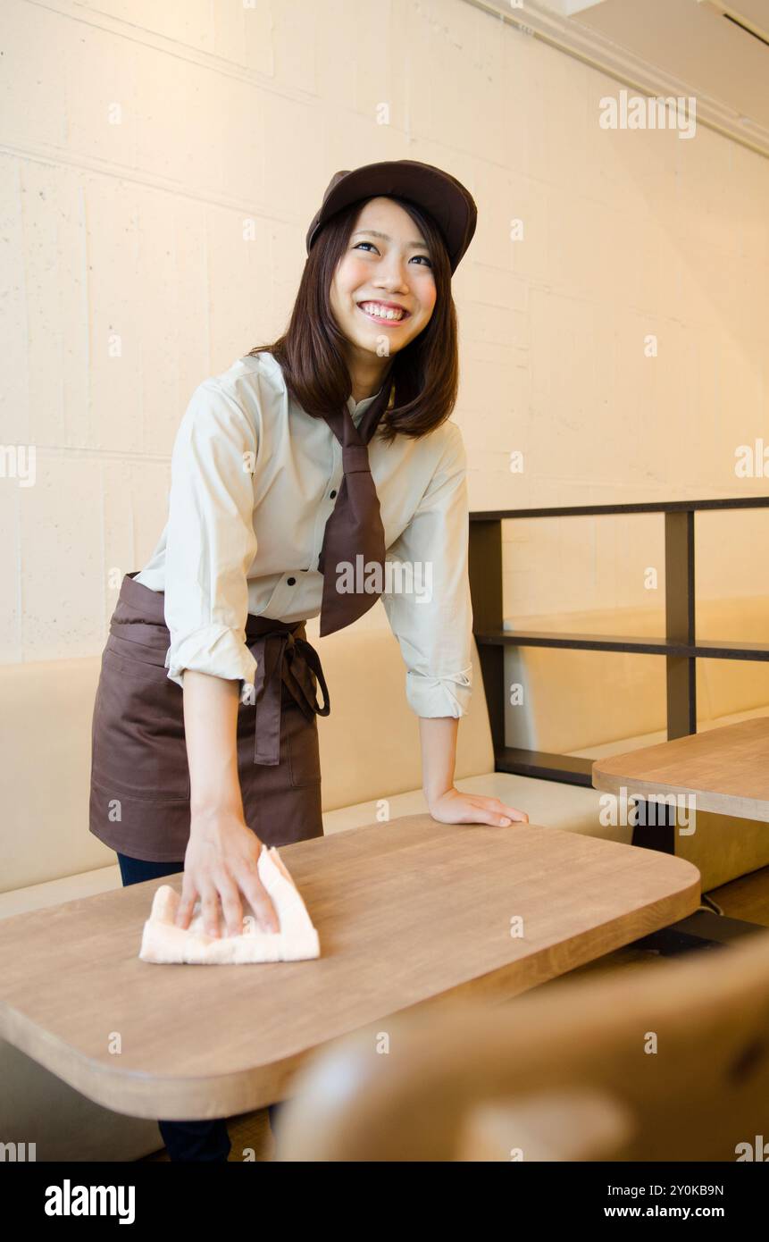 donna in uniforme che pulisce il tavolo Foto Stock