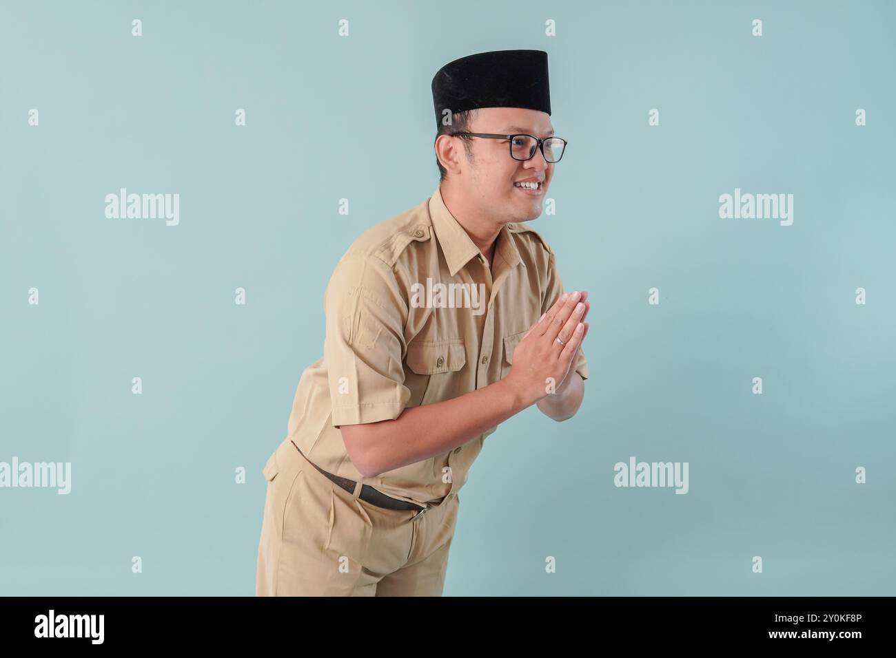 Educato lavoratore del governo indonesiano che fa un gesto di saluto sorridente, isolato da sfondo blu. Concetto di funzionario pubblico PNS. Foto Stock