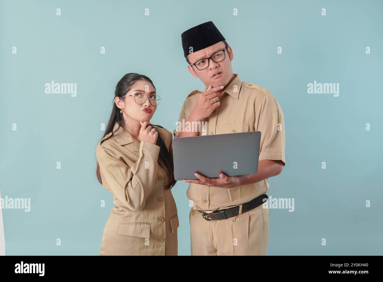 Una premurosa coppia di impiegati governativi che indossa l'uniforme kaki che tiene il computer portatile e che pensa seriamente al compito. PNS e concetto di funzionario pubblico. Foto Stock