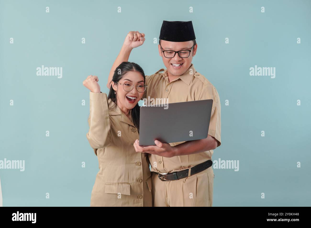 Due entusiasti impiegati governativi indonesiani che indossano l'uniforme kaki tenendo un laptop con un'espressione felice di successo. PNS e concetto di funzionario pubblico. Foto Stock