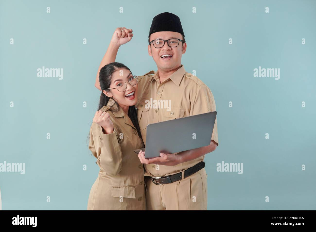 Due entusiasti impiegati governativi indonesiani che indossano l'uniforme kaki tenendo un laptop con un'espressione felice di successo. PNS e concetto di funzionario pubblico. Foto Stock
