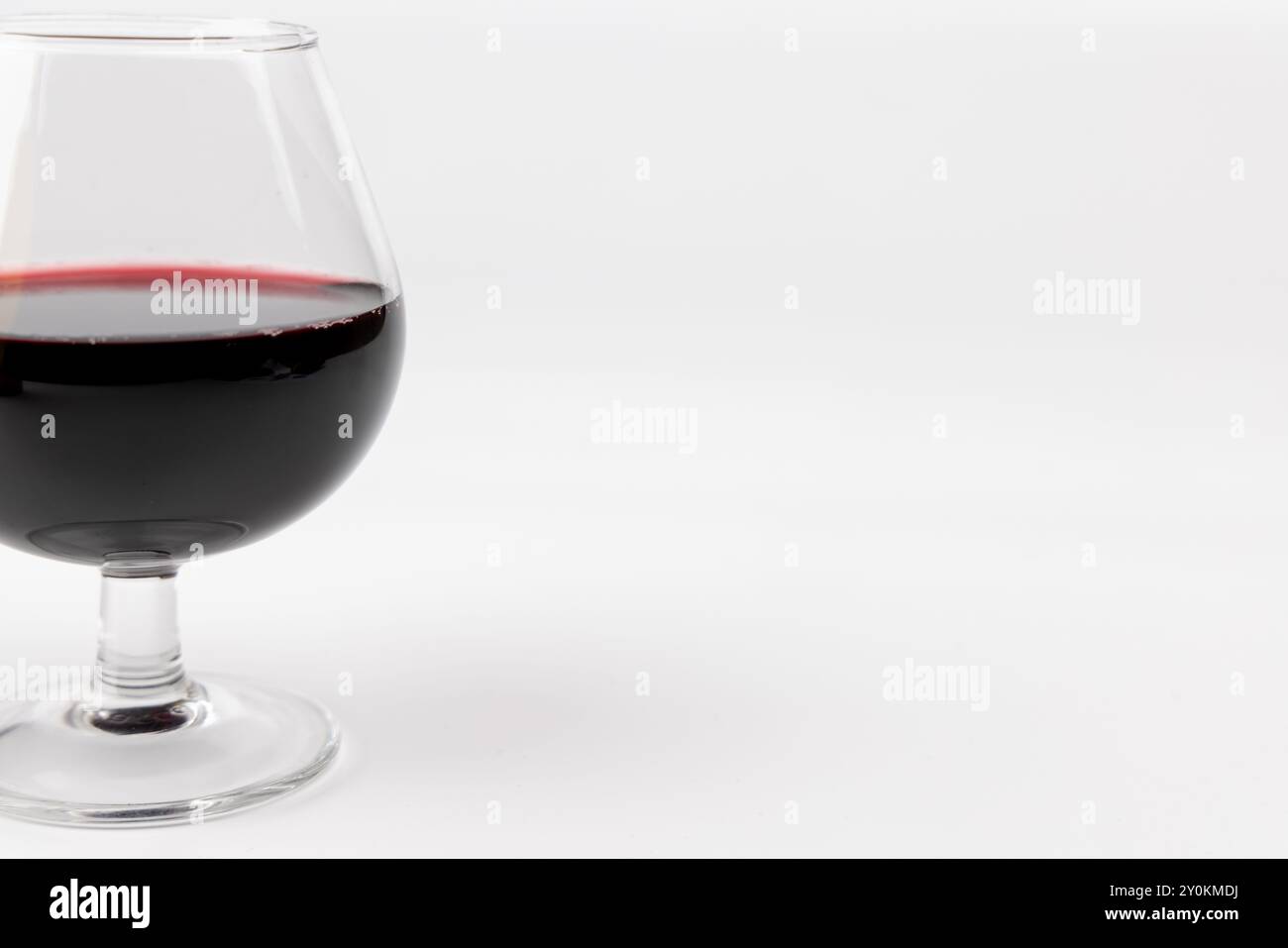 Un bicchiere di vino pieno di vino rosso, posto sul lato sinistro dell'immagine su un semplice sfondo bianco. La foto è orientata orizzontalmente Foto Stock