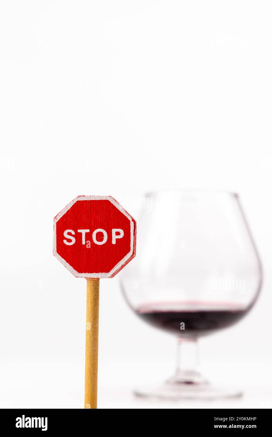 Uno scatto verticale con un segnale di stop in legno con dettagli nitidi, con un bicchiere di vino posizionato dietro di esso. Lo sfondo bianco migliora la messa a fuoco sulla S. Foto Stock