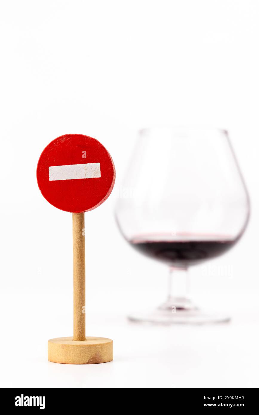 Una foto verticale incentrata su un cartello di legno "No Entry" centralmente. Dietro di esso, un bicchiere di vino è sottilmente fuori fuoco su uno sfondo bianco puro, cr Foto Stock