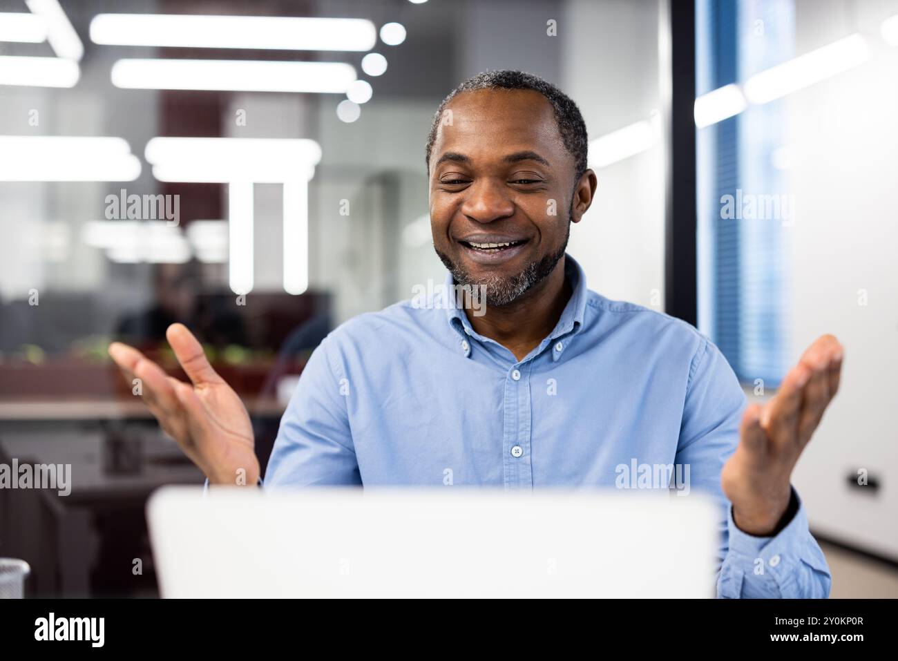 Un uomo d'affari sicuro partecipa alle videochiamate utilizzando un laptop in ufficio. Esprime felicità ed entusiasmo durante una conversazione vivace. Ideale per concetti di comunicazione e lavoro di squadra Foto Stock