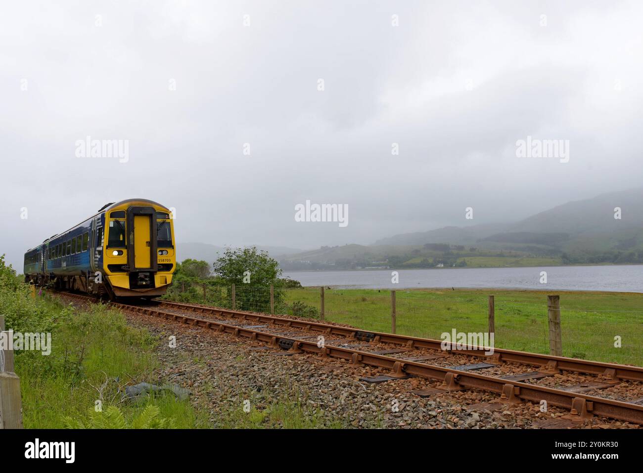 Il treno ScotRail DMU 158703 passa lungo la costa di Loch Carron sulla linea Kyle, giugno 2024 Foto Stock