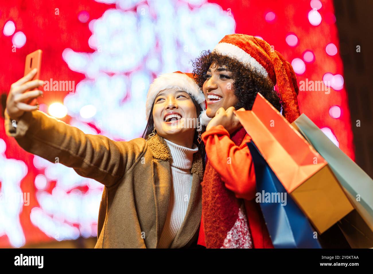 Due amici felici che scattano selfie mentre tengono le borse della spesa la sera di natale Foto Stock