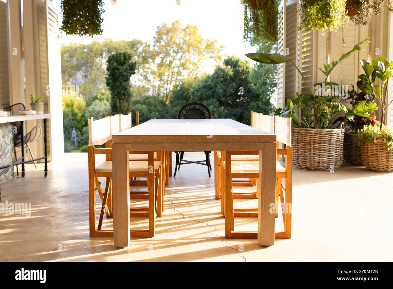 Tavolo da pranzo con sedie in legno nel patio illuminato dal sole, circondato da lussureggiante vegetazione Foto Stock