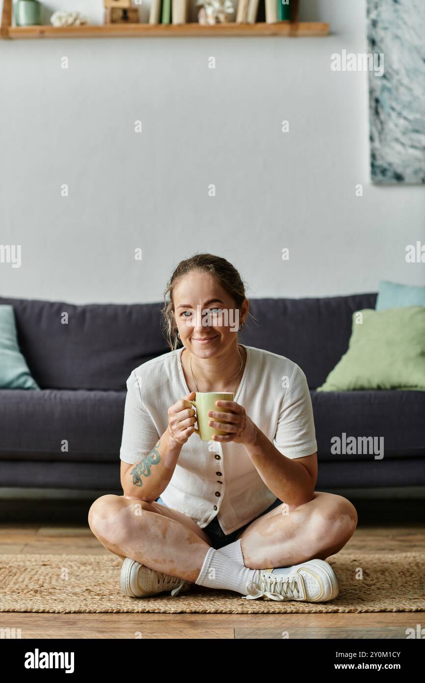 Una donna sorseggia una bevanda calda mentre è seduta comodamente sul pavimento. Foto Stock