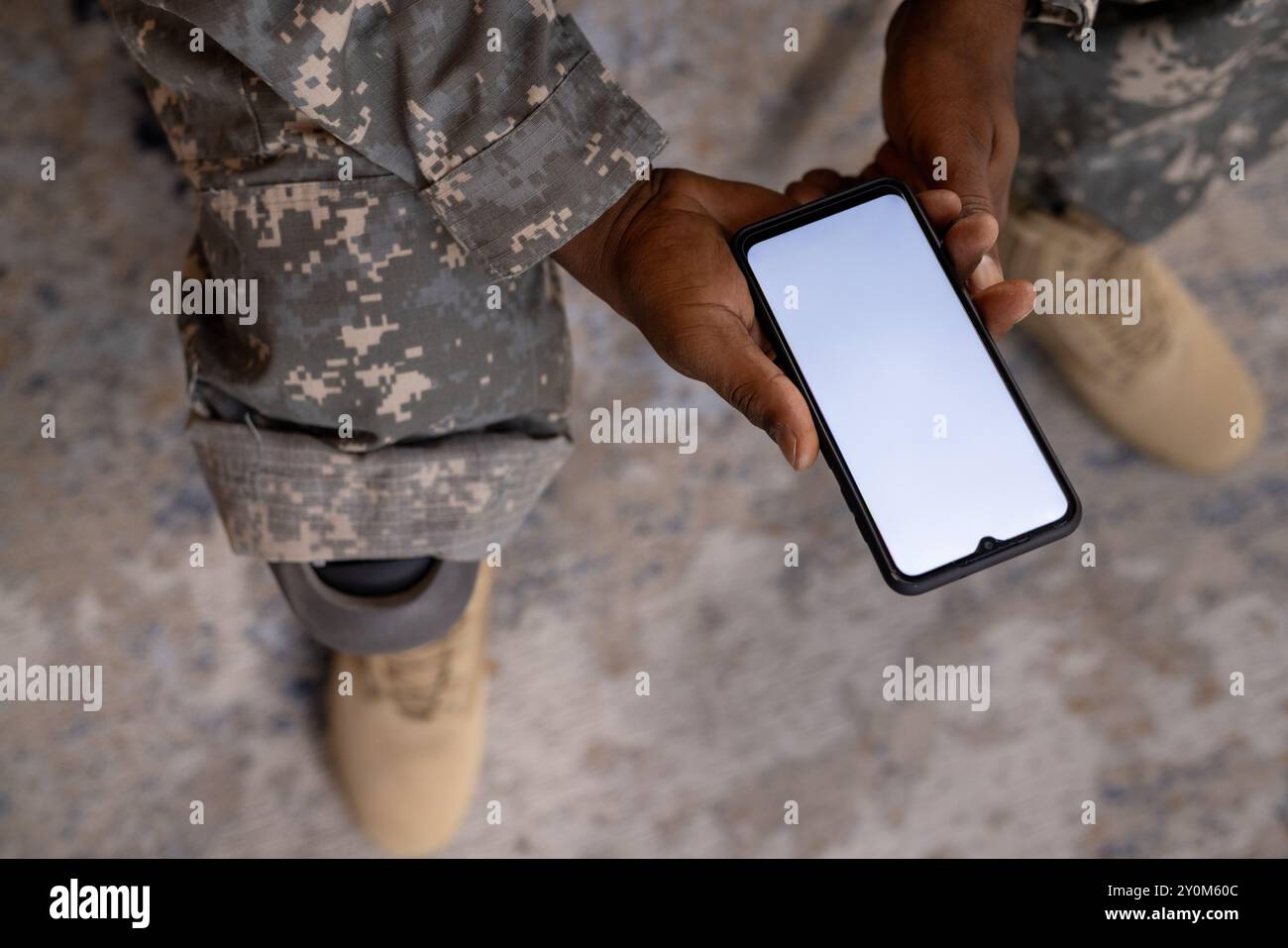 Tenendo in mano lo smartphone, la persona in uniforme militare con protesi alle gambe sedute, spazio di copia Foto Stock
