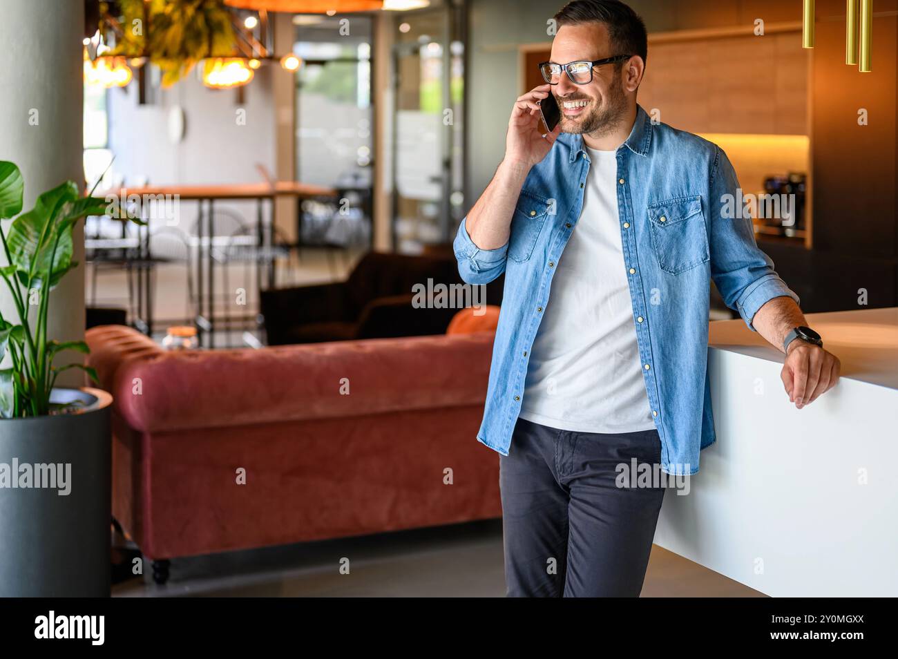 Ritratto di un venditore sorridente in occhiali che comunica tramite smartphone mentre si trova in ufficio Foto Stock